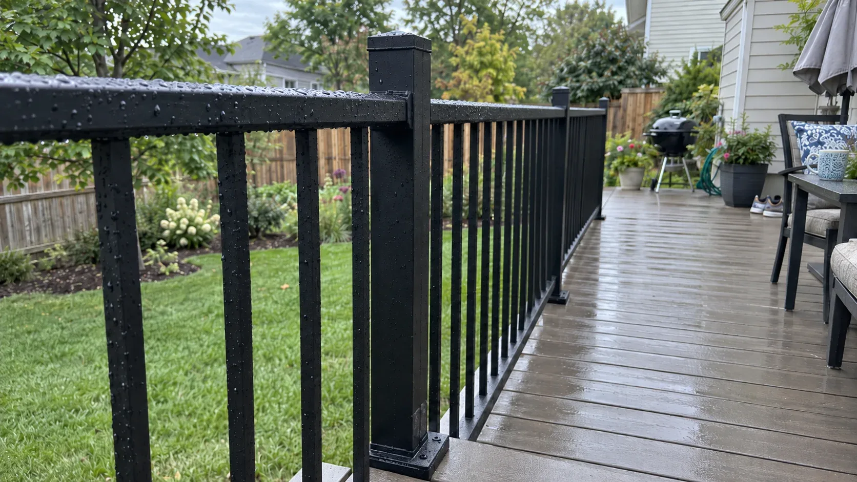 A finished composite deck with black aluminium railings and stairs, decking and railing samples laid across the boards beside a set of plans